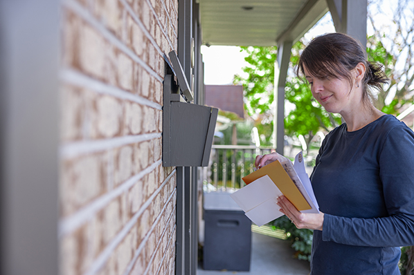 Woman standing on the patio of her brick house, looking at her mail. 